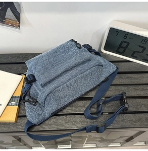 Detailed view of blue denim sling bag with adjustable strap and durable buckles on wooden table