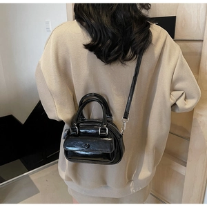 Glossy black patent leather handbag with dual handles and long shoulder strap on model