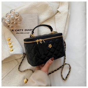Detalle del bolso vanity acolchado negro con motivo de camelia dorada y cadena oro