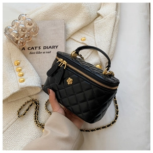 Detalle de bolso tipo cubo acolchado negro con cadena dorada y detalle de flor metal