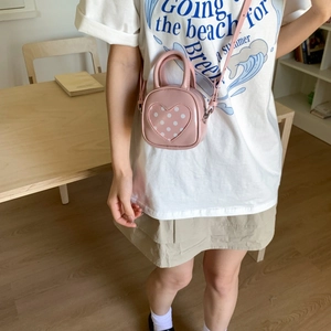 Detail of pink mini bucket bag with heart polka dots worn on a casual white t-shirt