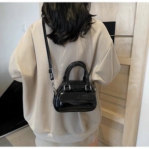 Detail view of a black glossy crossbody bag with round handles and a front pocket