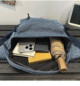 Internal capacity of denim sling bag holding phone, power bank, notebook, and umbrella