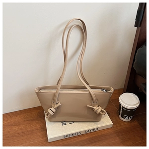 Détail d'un sac fourre-tout en cuir crème avec fermeture éclair et nœuds décoratifs sur la sangle