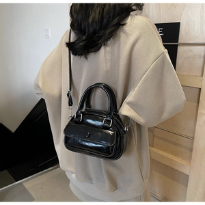 Detail of black glossy mini Boston bag with double handles and adjustable crossbody strap