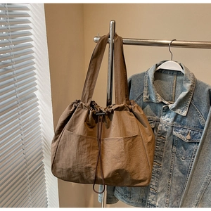 Brown drawstring tote bag with pleated nylon texture and large front pocket on metal rack