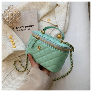 Detalle de bolso cubo acolchado verde menta con cadena dorada y logotipo de flor