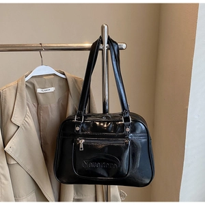 Detail of black patent leather tote bag featuring Nononono embossed logo and front zipper