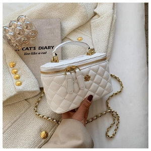 Detalle de bolso bandolera blanco acolchado con cierre de flor dorada y cadena sobre tweed