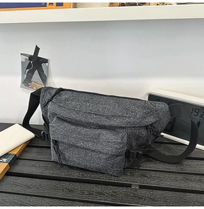 Detail view of washed gray denim sling bag with multi-compartment zippers and buckle strap