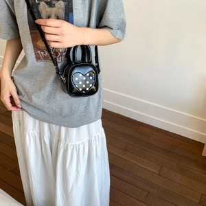 Detail of black mini PU leather bucket bag with white polka dot heart on crossbody strap