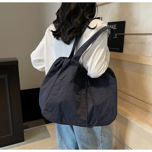 Deep blue nylon tote bag with drawstring closure and wide strap shown on model's shoulder