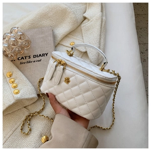 Detalle del bolso de cubo acolchado blanco con logo de camelia dorada y asa de cadena