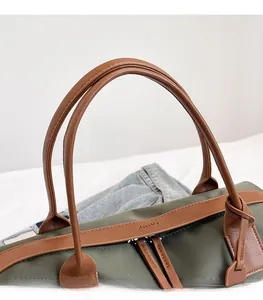 Detail of olive green tote bag featuring brown leather handles and dual metal zippers