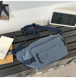 Close-up of blue washed denim sling bag with zipper pockets and adjustable buckle strap