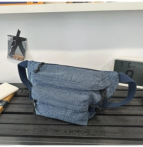 Detailed close-up of blue washed denim chest bag featuring dual zippers and plastic buckle