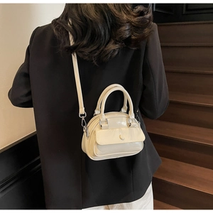 Model showing cream patent leather shell bag with adjustable strap on stairs