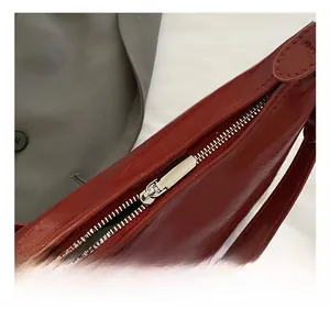 Detail of silver metal zipper on burgundy oil wax leather underarm bag with glossy finish