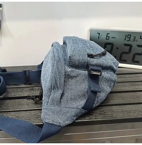 Detail view of washed denim sling bag showing navy blue adjustable strap and side layers