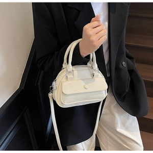 Detail of cream white mini bowling bag featuring a front pocket and glossy patent finish