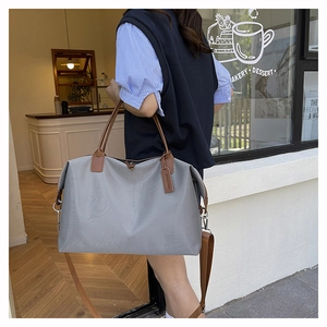 Detail of grey tote bag with brown leather handles and adjustable shoulder strap on a table