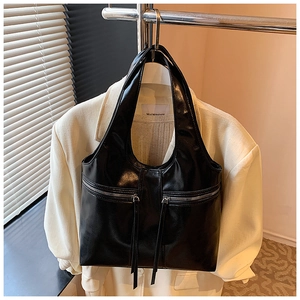 Détail d'un sac à main noir en simili cuir huilé avec poches zippées symétriques et glands