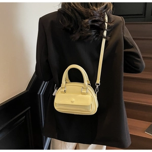 Mini cream leather pillow bag with top handle and round buckle detail shown on a model