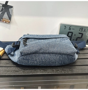 Detail view of washed blue denim chest bag showing side structure and adjustable strap