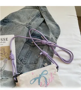 Detailed view of the small beige canvas crossbody bag with blue bow and pink embroidery