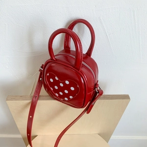Detail of red mini handbag featuring a heart-shaped polka dot pattern on wood surface