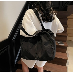 Detail of a large black tote bag with drawstring closure and wide strap on a model