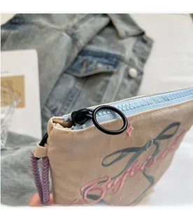 Detail shot of smooth light blue zipper and embroidered lettering on beige nylon shoulder bag