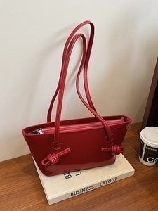 Sac cabas en cuir verni rouge avec bandoulière nouée sur un bureau au style minimaliste