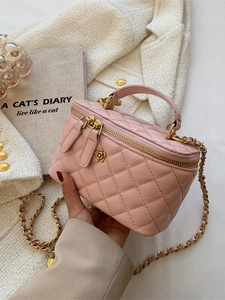 Bolso cubo acolchado rosa con cadena dorada y detalle floral sostenido en la mano