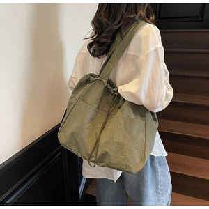 Detail of olive green large capacity shoulder bag with drawstring and front pocket design