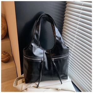Détail d'un sac cabas noir brillant avec poches zippées en métal et longues franges en cuir
