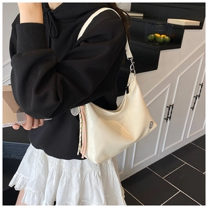 Detail of a creamy white glossy PU leather crescent bag with stylish tassel and shoulder strap