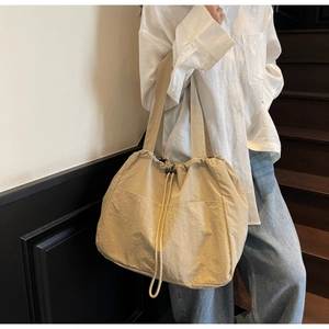Detail of beige large tote bag featuring drawstring closure and two front pockets