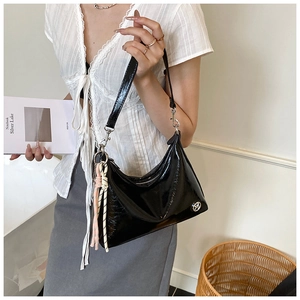 Detail of a black glossy leather shoulder bag with silver chain and woven pendant