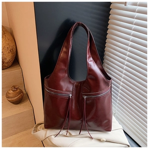Détail d'un sac cabas en cuir bordeaux avec poches zippées et pompons décoratifs élégants
