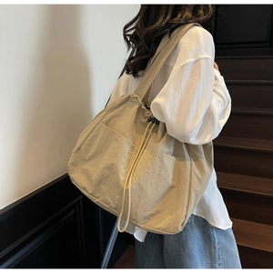 Detail view of a large capacity beige nylon tote bag with drawstring closure and outer pockets