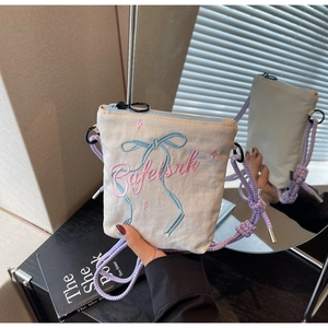 Detail of canvas mini bag featuring bow embroidery and purple woven shoulder strap