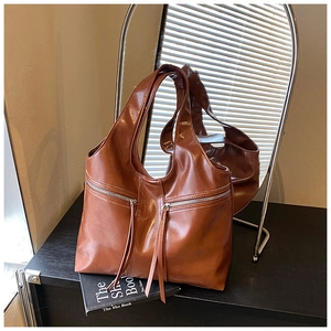Détail du sac cabas marron foncé avec longs zips à franges et texture cuir huilé brillant