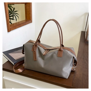 Close-up of large taupe tote bag with brown leather handles and brown strap on wood