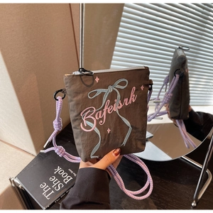 Detail of brown crossbody bag with pink lettering and blue bow embroidery on fabric