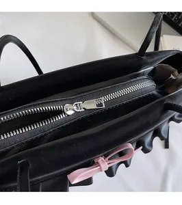 Gros plan d'un sac sous les aisselles en cuir noir avec zip argenté et nœud rose décoratif
