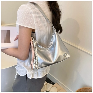 Silver crescent hobo bag shown on shoulder featuring metallic finish and woven charm detail