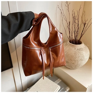 Détail d'un sac bandoulière en cuir brillant caramel avec décorations de zips à glands