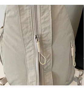 Detailed close-up of a smooth nylon zipper and matte pull cord on a beige crossbody bag