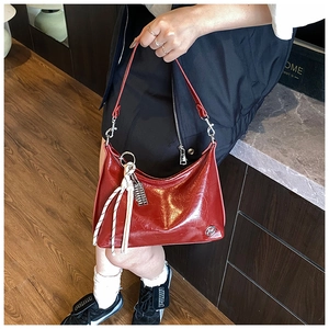 Detail view of red oil-wax leather shoulder bag with woven knot charm and metal logo